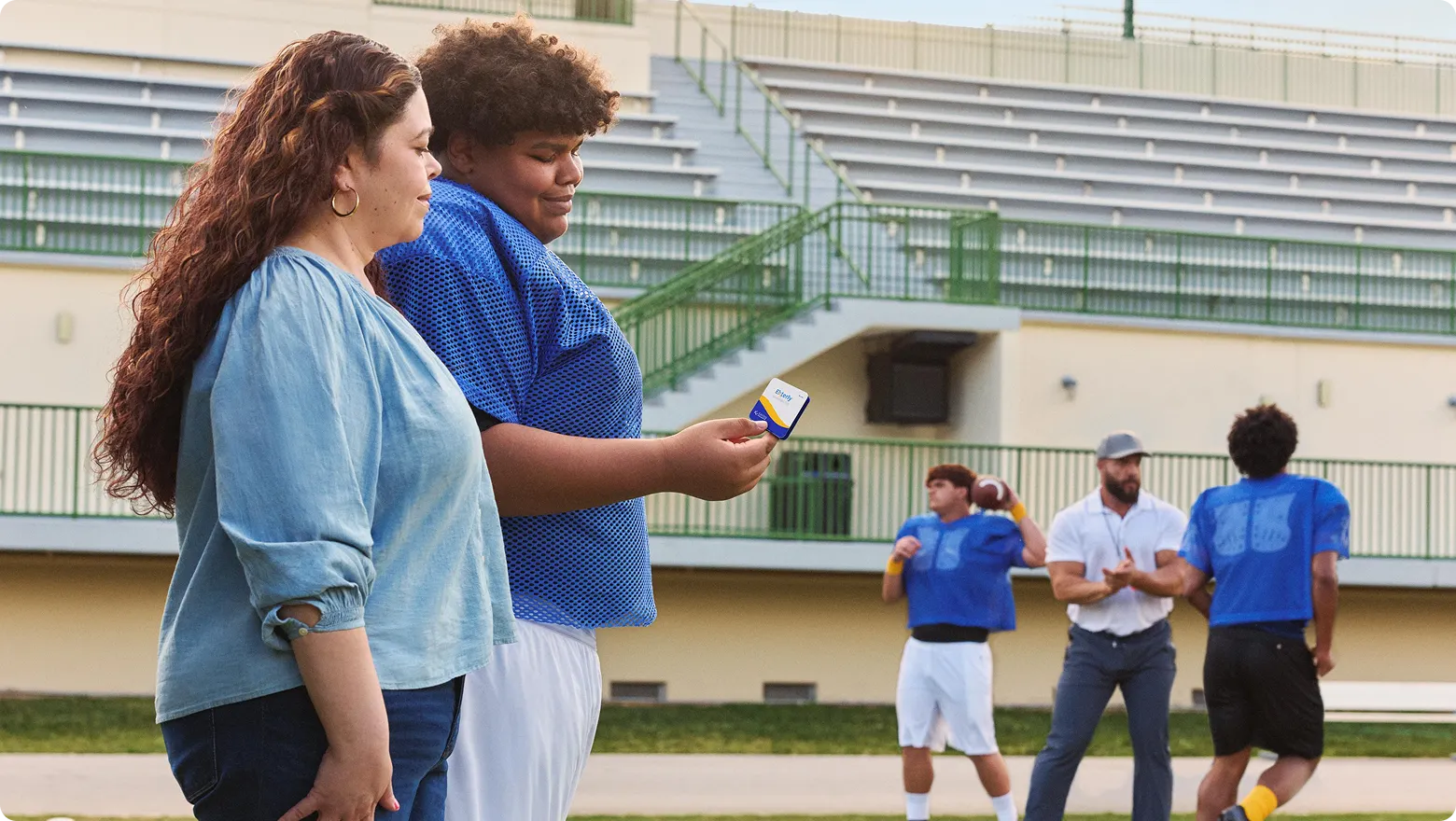 Real EKTERLY® (sebetralstat) patient Ellis holding EKTERLY® medication while walking with his mother at football practice